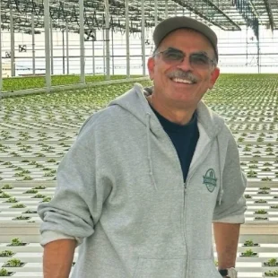 Cheerful man in a greenhouse proudly tending to healthy plants in a light gray hoodie.