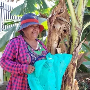 Cheerful woman with banana tree, vibrant greenery, and colorful attire in sunny garden setting.